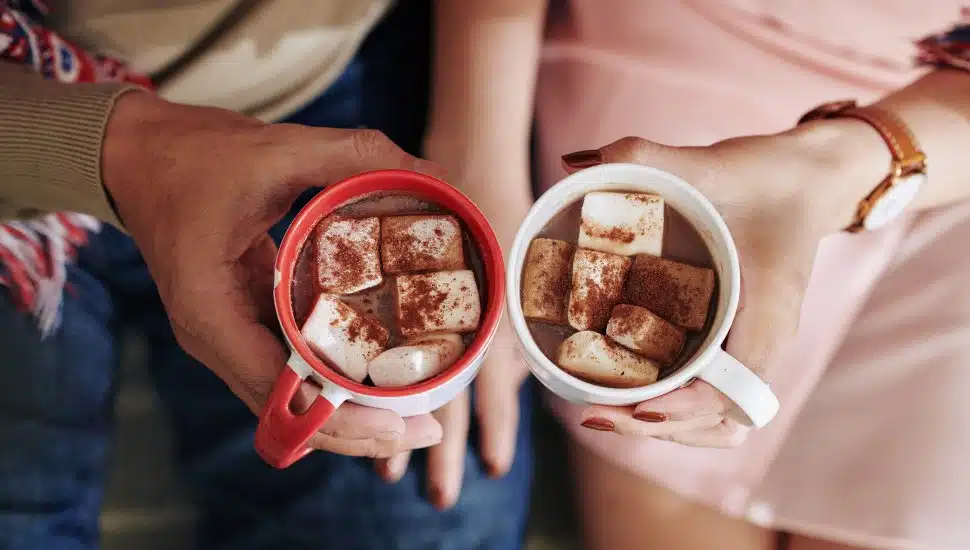 Couple holding cups of hot chocolate with marshmallows.