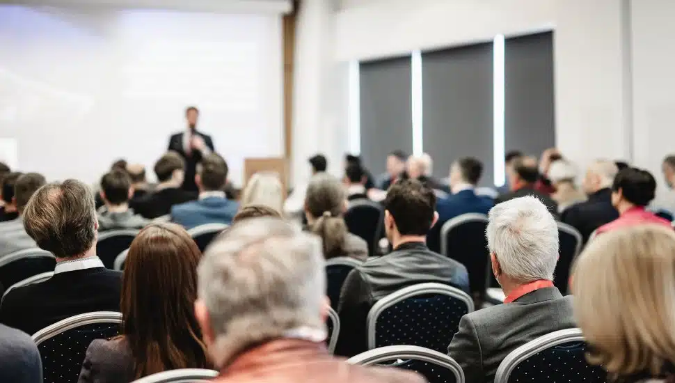 Person presenting at front of room to an audience.