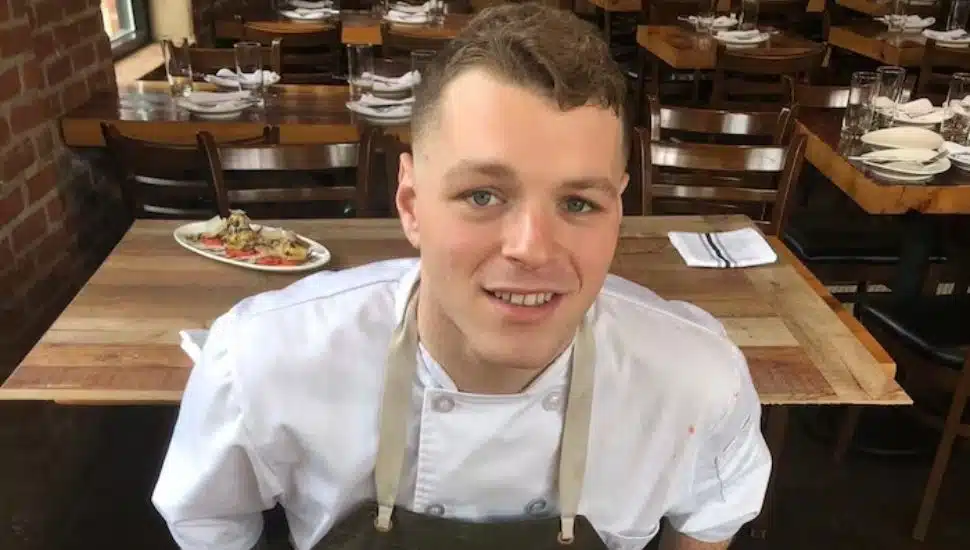 Alessandro Fiorello in a chef uniform with tables behind him.