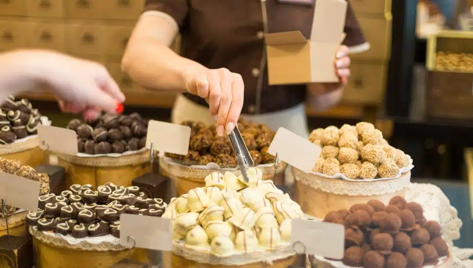 A server using tongs to pack a chocolate box at a chocolate shop.