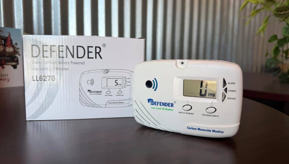 Defender LL6270 low-level carbon monoxide monitor displayed with packaging on a table, featuring a digital CO PPM readout and test/reset buttons.