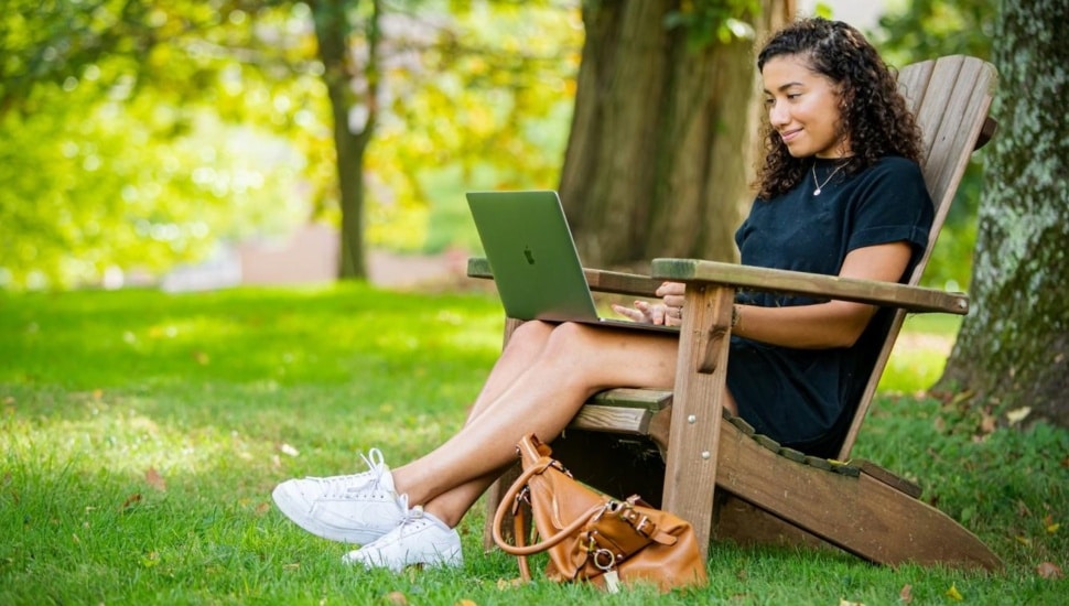 Female college student works on laptop computer while sitting outside.