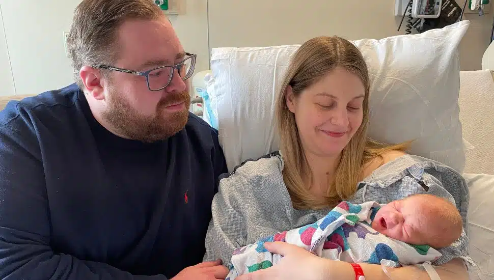 Parents smile as they hold their newborn baby in a hospital room shortly after birth.