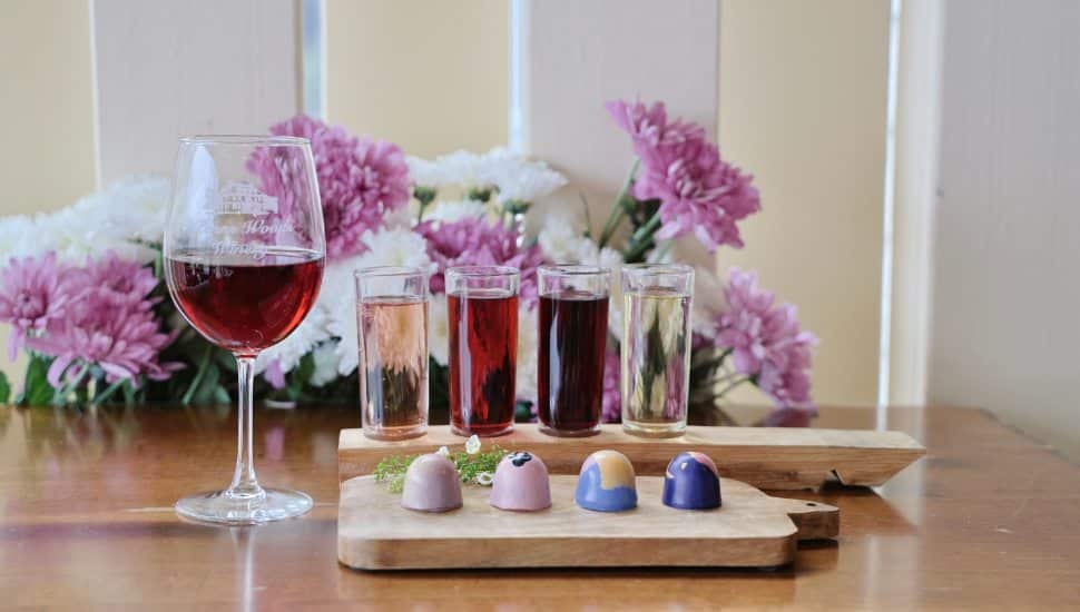 A wine tasting flight next to a plate of colorful chocolates.