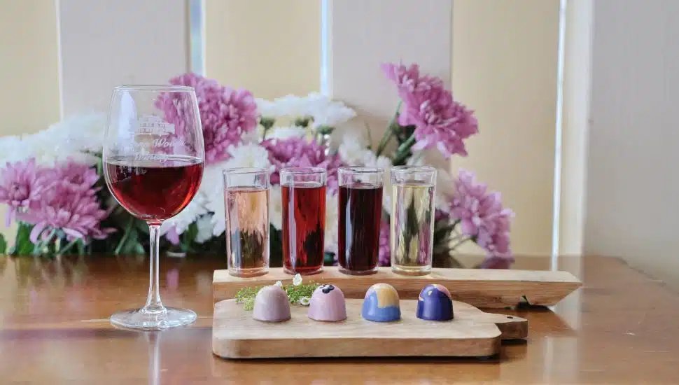 A wine tasting flight next to a plate of colorful chocolates.