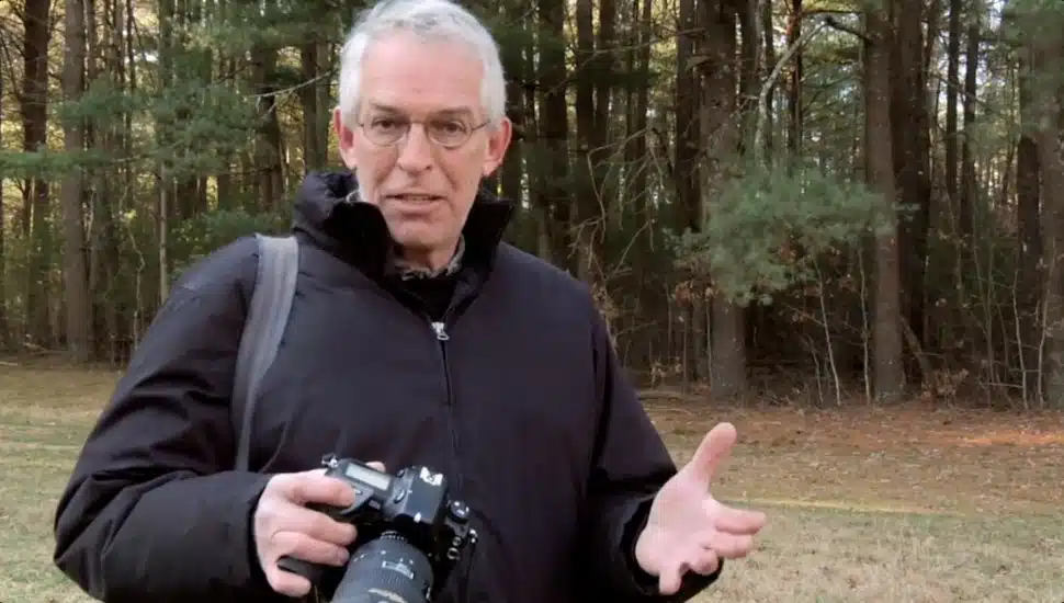 Robert Caputo holding a camera with woods in background.