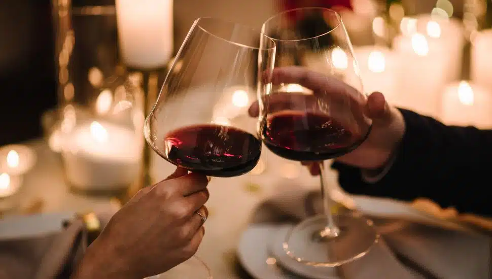 Couple clink wine glasses together at romantic dinner.
