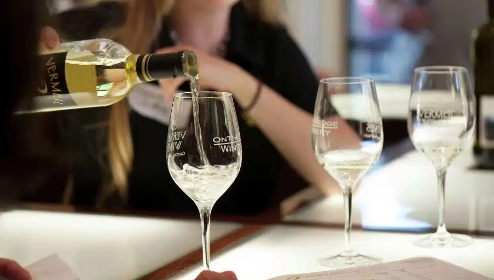 A hand pouring a glass of Vermeil Wine at a tasting event.