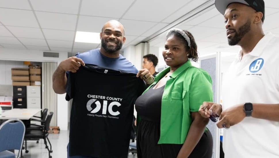 Philadelphia Eagles legend Brandon Graham stands with Chester County OIC staff members during a community event, holding a Chester County OIC T-shirt.