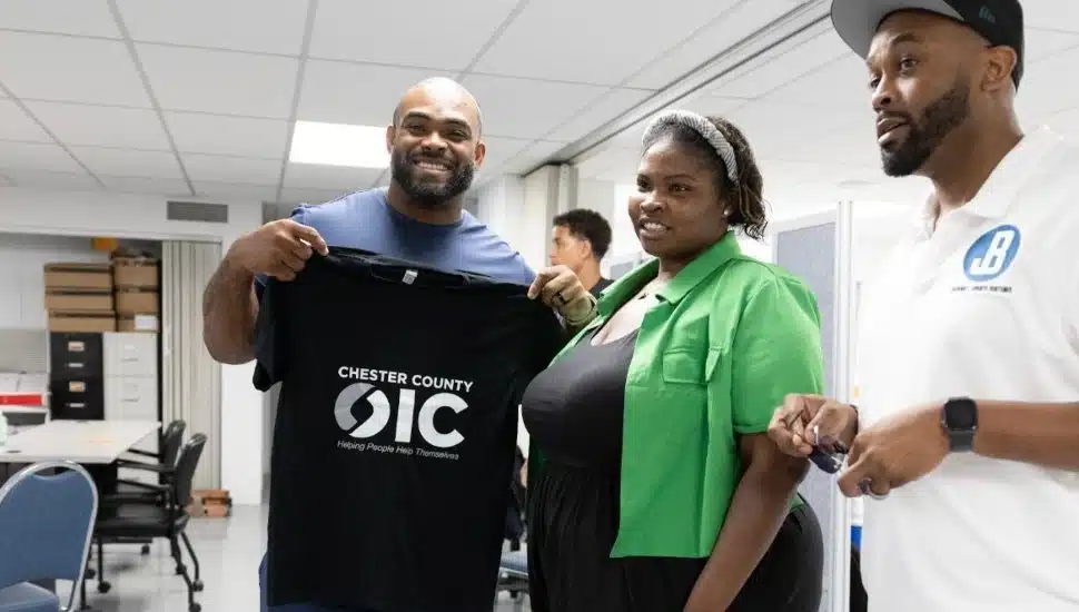 Philadelphia Eagles legend Brandon Graham stands with Chester County OIC staff members during a community event, holding a Chester County OIC T-shirt.