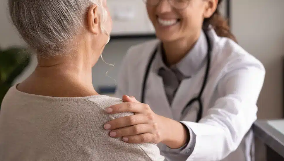 Close up back view smiling doctor touching mature patient shoulder.
