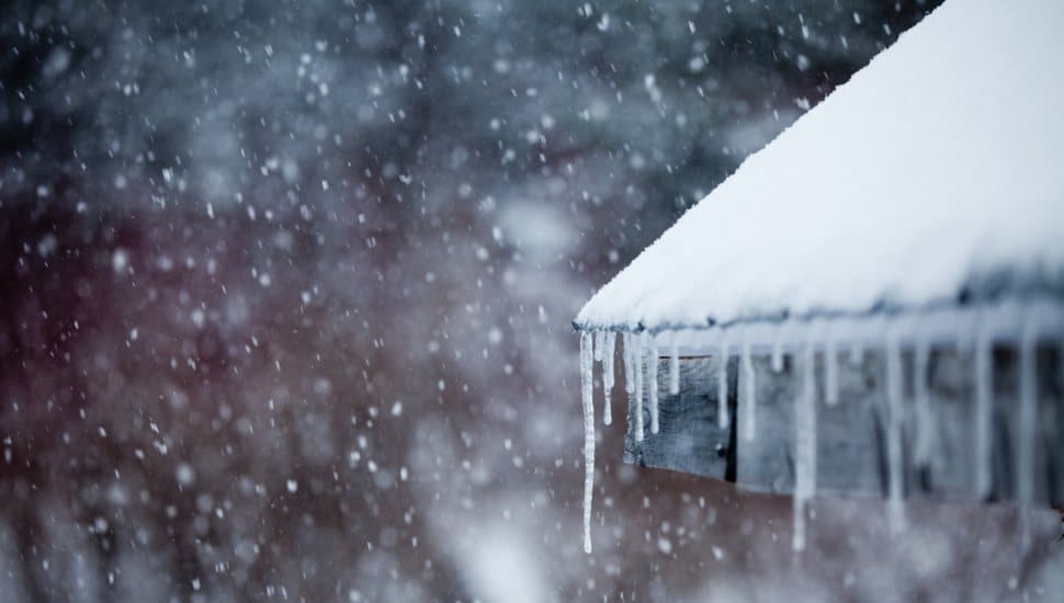 Icicles forming along the edge of a snow-covered roof during freezing winter weather, highlighting conditions that can lead to frozen water pipes.