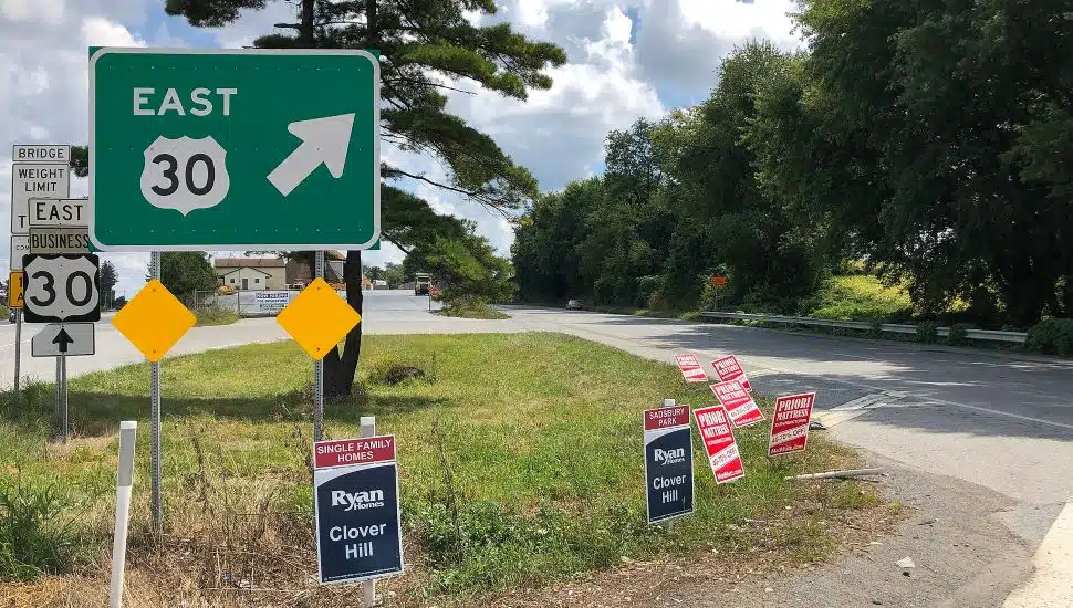 Route 30 green signage on a part of grass with political signs in ground.