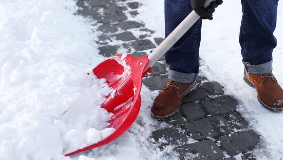 Man removing snow with shovel outdoors, closeup.