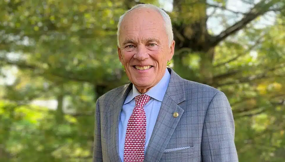 Gary Smith upper body headshot wearing suit with green nature background.