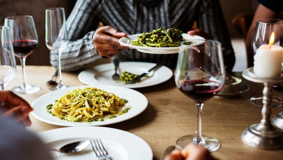 Two patrons enjoying plates of pasta alongside wine glasses and candles.