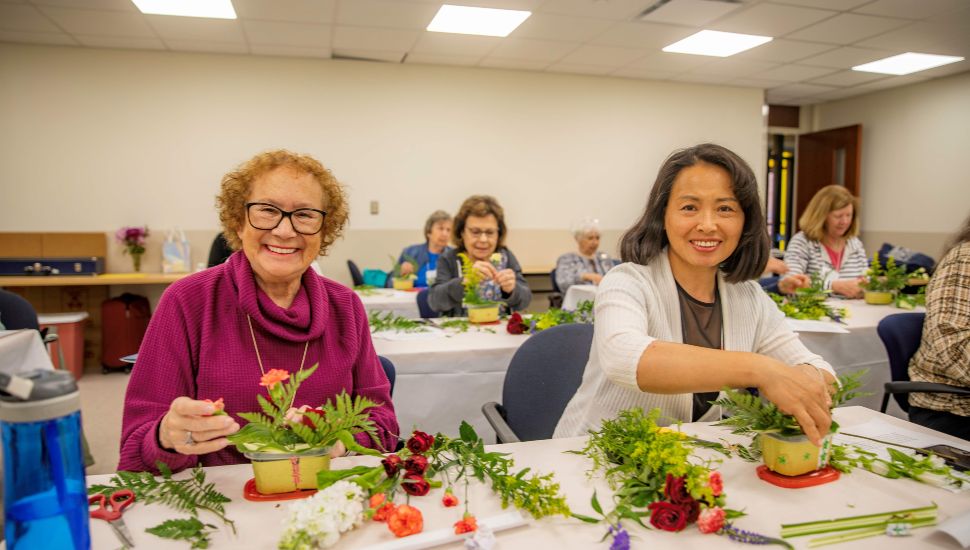 Adults participate in a floral design workshop at Delaware County Community College’s Return to Learn 55+ program, arranging flowers and greenery at tables in a classroom setting.