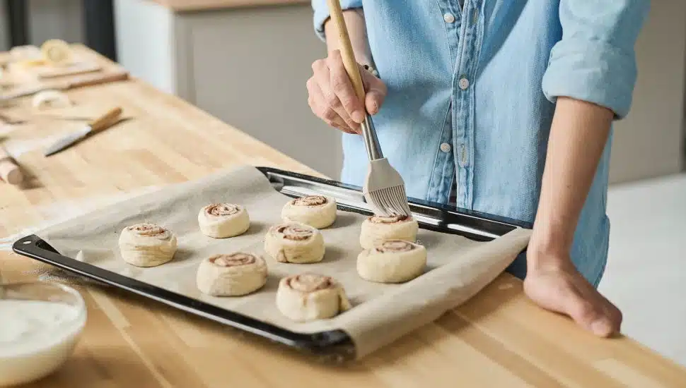 Woman making cinnamon buns on sheet pan.