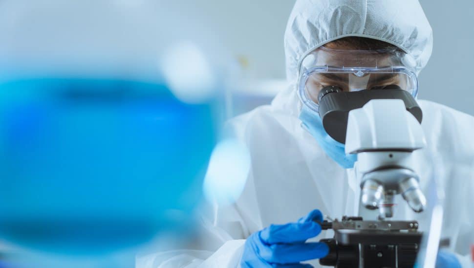 Researcher looks in the microscope wearing PPE gear.