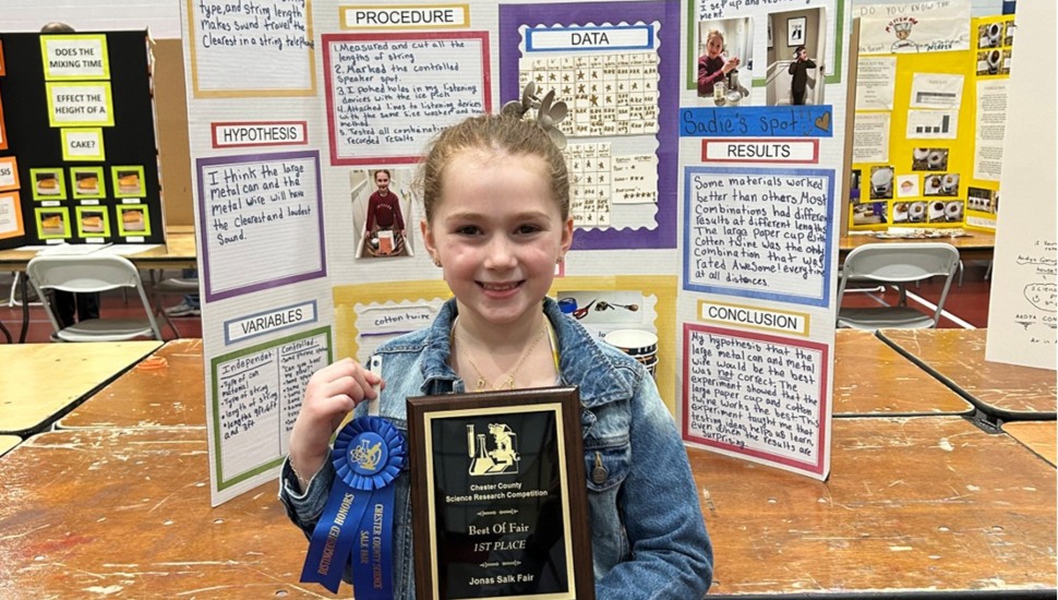 Elementary school student holds plaque and ribbon at science fair.