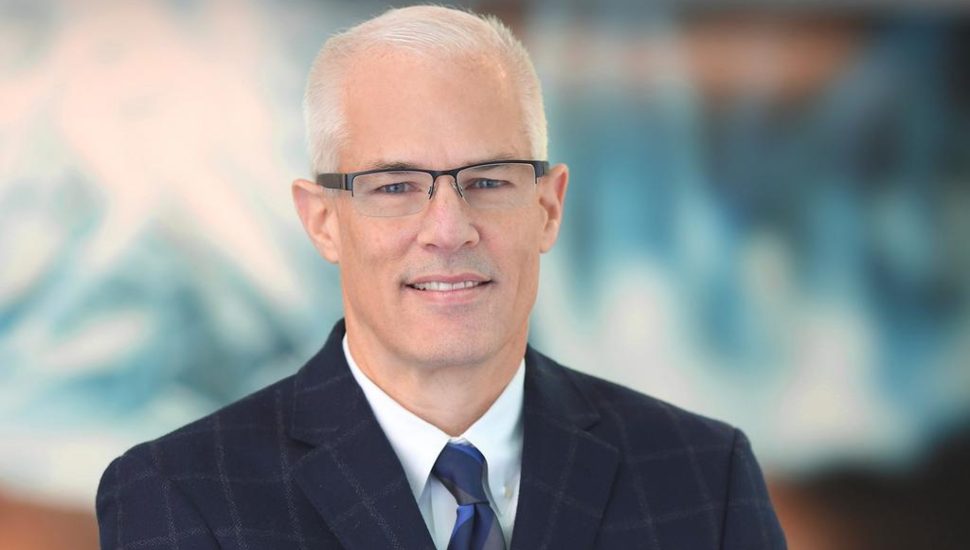 Dan Reuvers headshot, wearing suit and glasses with blurry blue background.