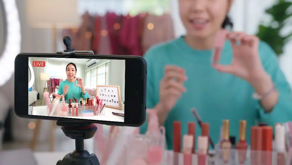 Woman films on phone for livestream shopping as she shows makeup.