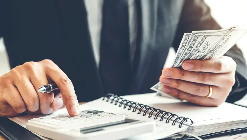 Businessman uses calculator with money in hand.