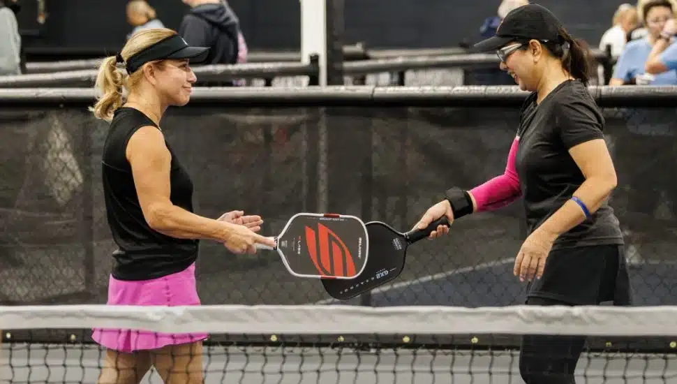 Two women players touch paddles while playing pickleball.