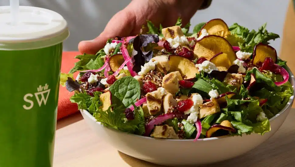 Saladworks bowl with green drink next to it.