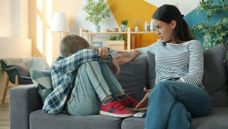 Young boy sits in frustration on the couch with his mother.