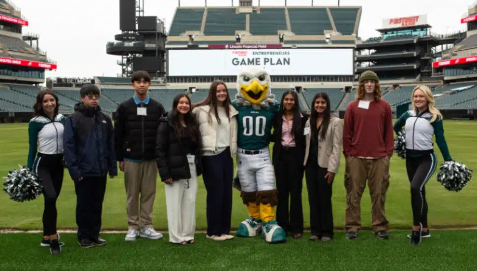 Students and Eagles mascot and cheerleaders pose for picture in football stadium.