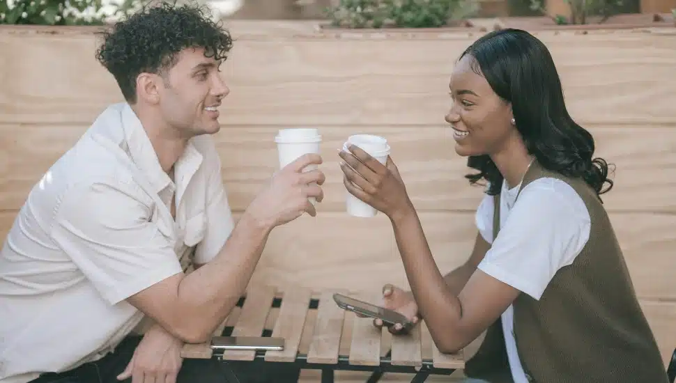 Young couple smile at each other while drinking coffee.