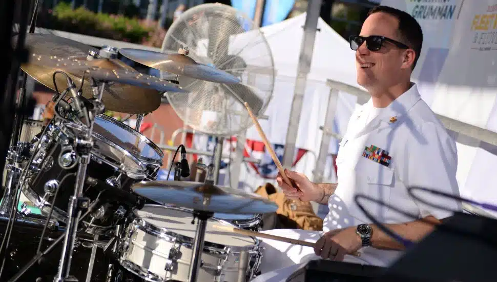 Chief Musician Joseph Ganzelli plays on the drums in white uniform.