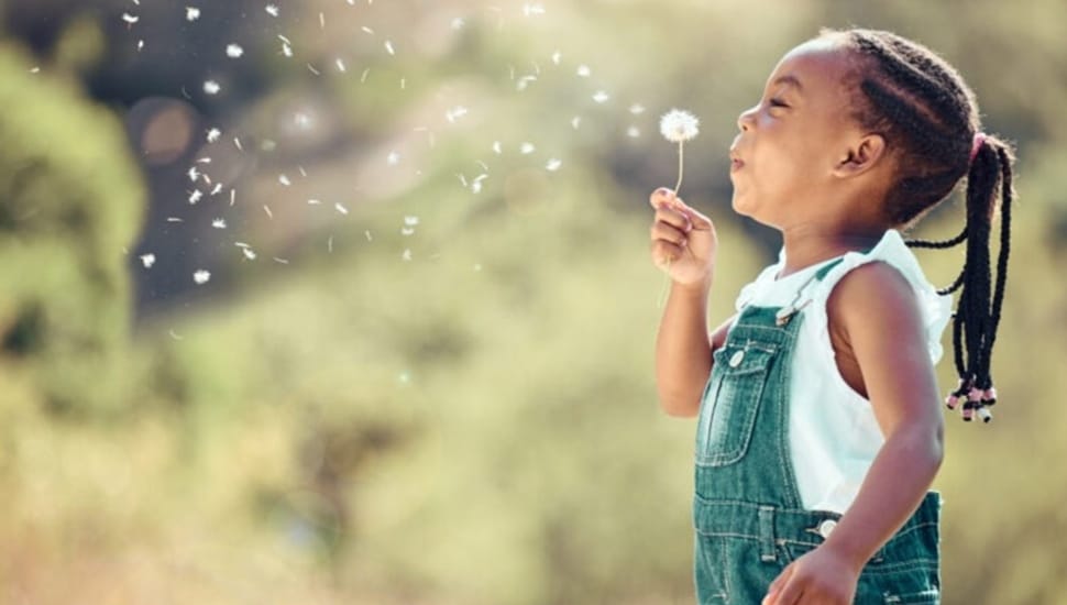 Little girl plays outside with flower.