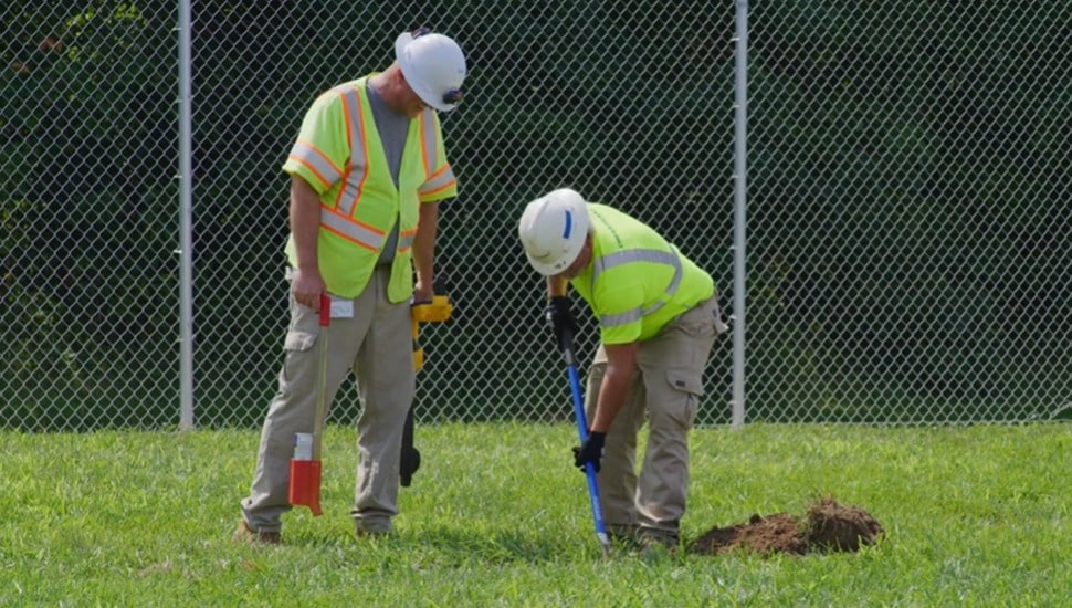 Two utility workers dig in the grass.