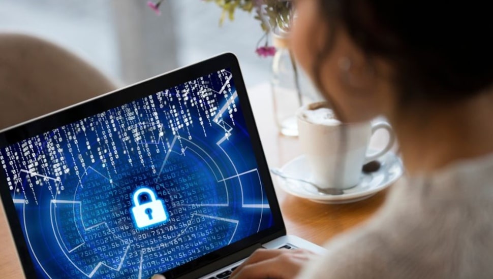 Woman looks at laptop with cybersecurity image on screen.