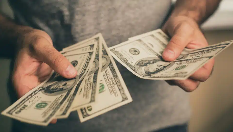 Man in gray shirt holds spread of money in hands.