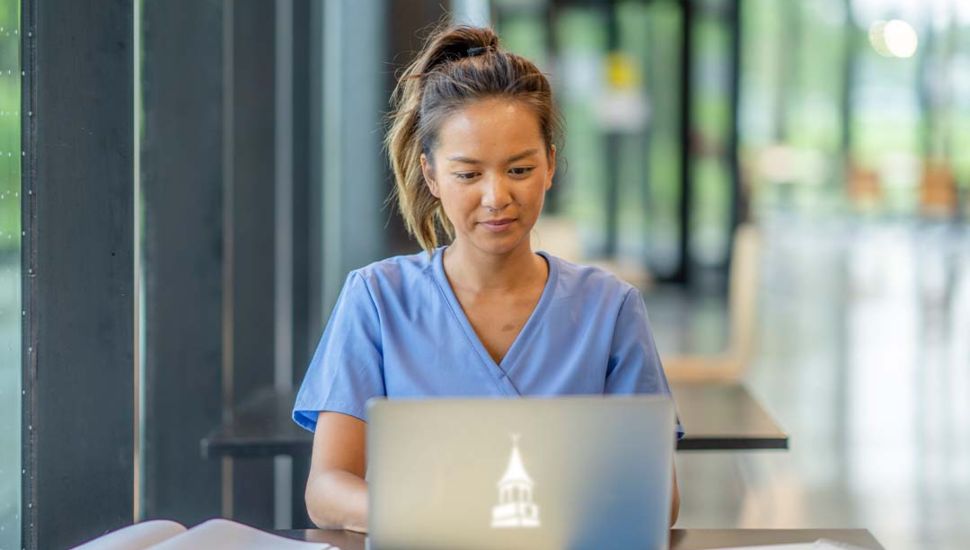 Nurse sitting in scrubs at laptop.