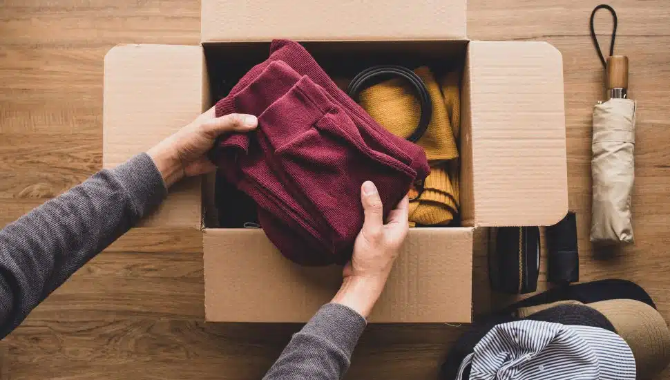 young person putting accessories clothing in brown box.