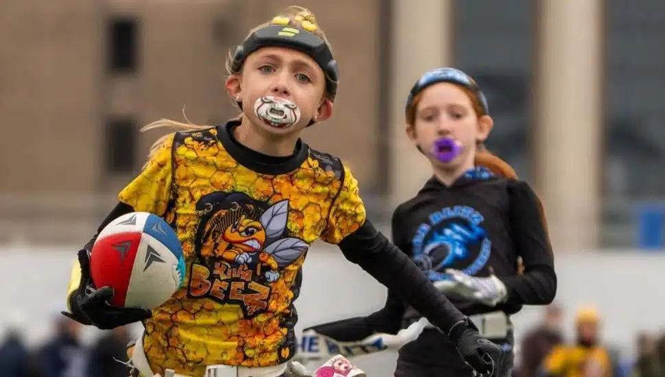 Young girls wearing uniforms and mouthguards playing flag football.