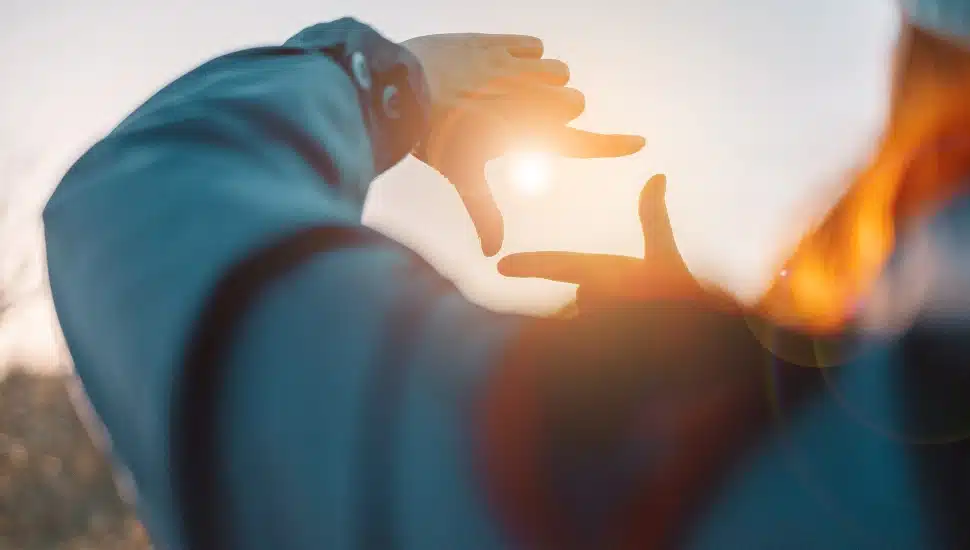 Closeup of female hands making frame gesture with sunrise on an autumn meadow at sunset with sun.