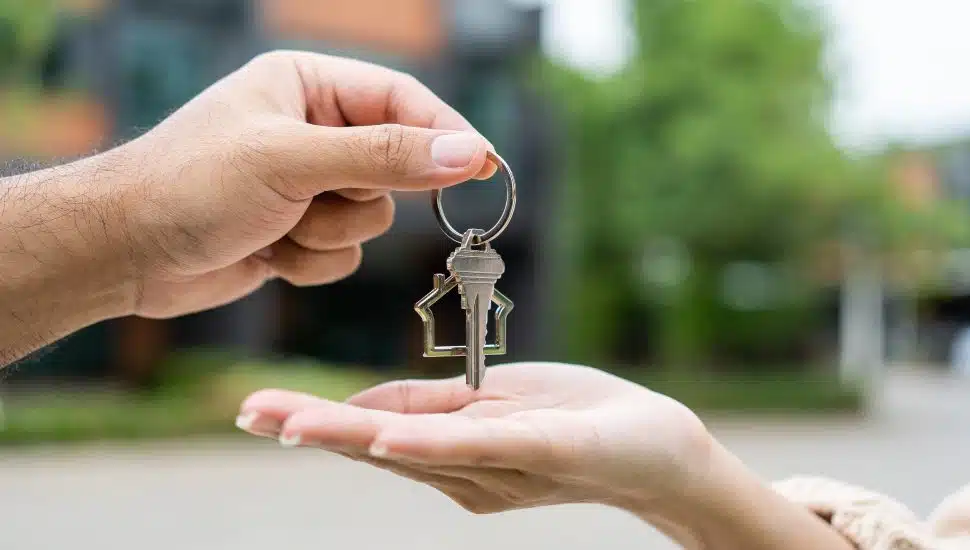 Person handing house key over to another person. New home homeownership.