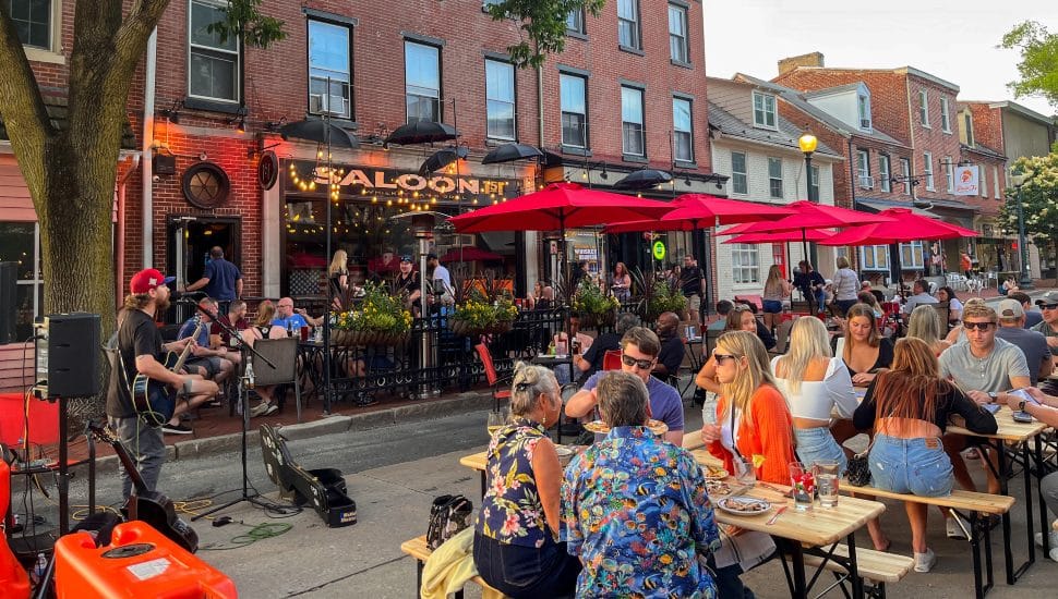 People dining outside at outdoor tables with umbrellas in streets of West Chester.