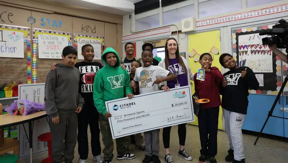Special education teacher is surrounded by her students as she receives giant check and award.