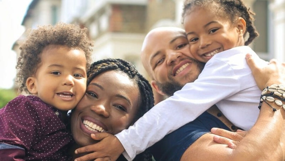 A smiling man and woman holding two young, happy children.