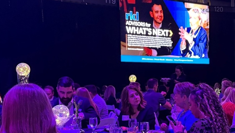 People eat dinner at an awards ceremony with a big screen monitor in the background.