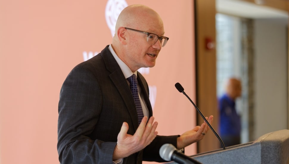 Middle-aged man in dark suit and glasses speaks at a podium at a conference.