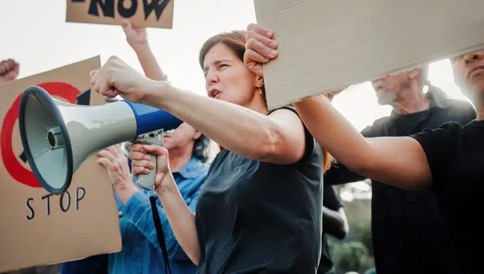 Stock image of people holding megaphones and posters at a rally.