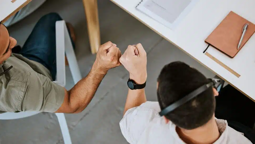 Two male employees fist bump each other at work.