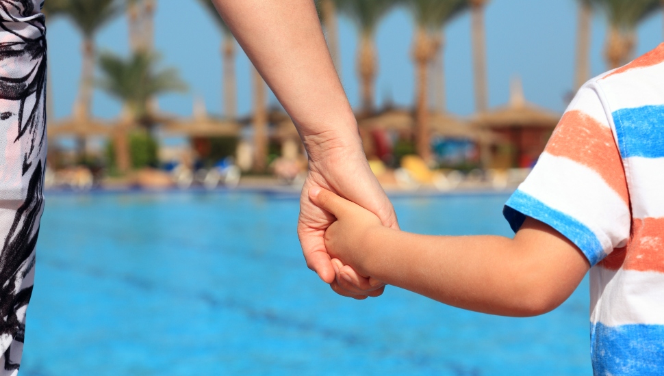 Mother and son holding hands on vacation looking at swimming pool concept for family vacations, child safety and single parent holiday.